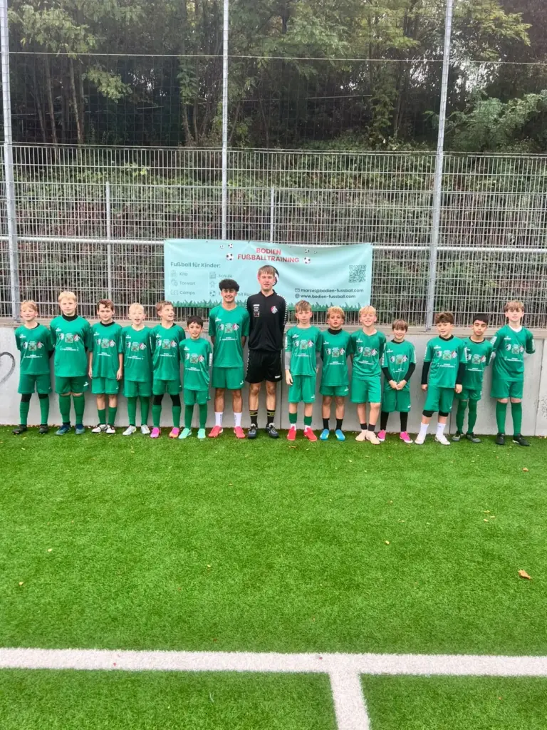 Gruppenfoto einer Trainingsgruppe in grünen Camp-Trikots mit Trainer am Rand des Kunstrasenplatzes