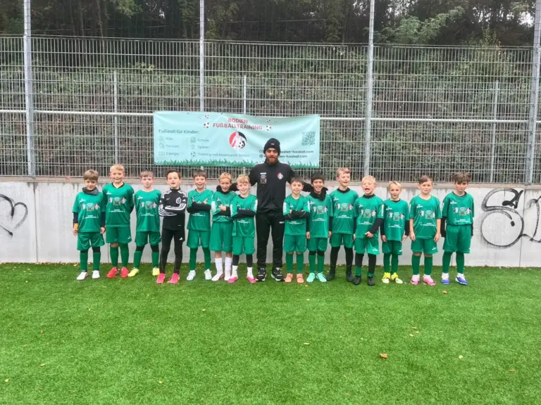 Gruppenfoto einer Trainingsgruppe mit Trainer in grünen Camp-Trikots vor dem Bodien-Fußballtraining-Banner